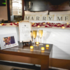 Wedding proposal decorations with candles, roses, photos and champagne arranged on and around bed