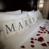 Marriage proposal decor with roses and candles on hotel room bed
