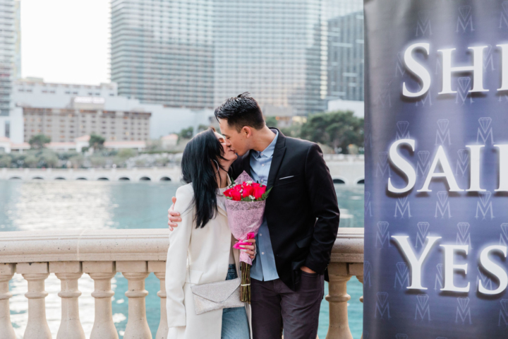 Couple kisses next to "She Said Yes" banner after marriage proposal at the Bellagio Fountains on the Las Vegas strip