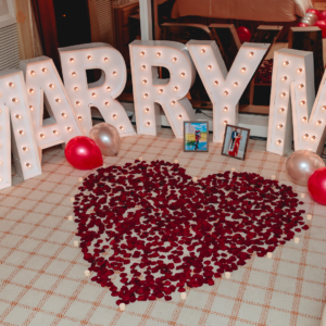 A large "marry me" sign, balloons, rose petals and candles decorating a Vegas hotel room with a romantic feel