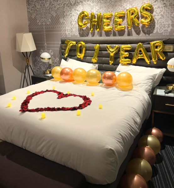 A las vegas hotel room is decorated for a romantic anniversary. Balloons and rose petals are placed throughout the room and bed.